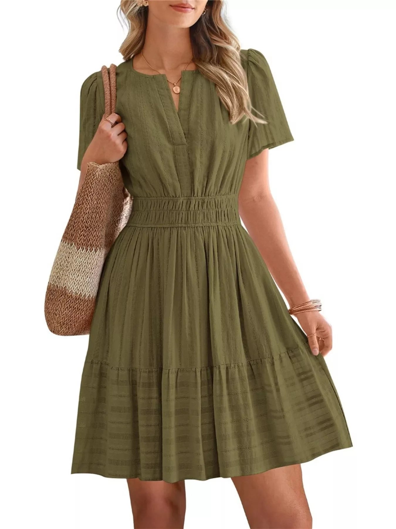 Woman wearing a green dress holding a striped bag on a white background