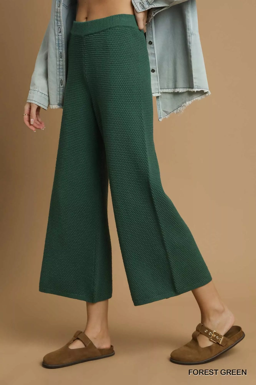 Person wearing forest green pants with a beige background
