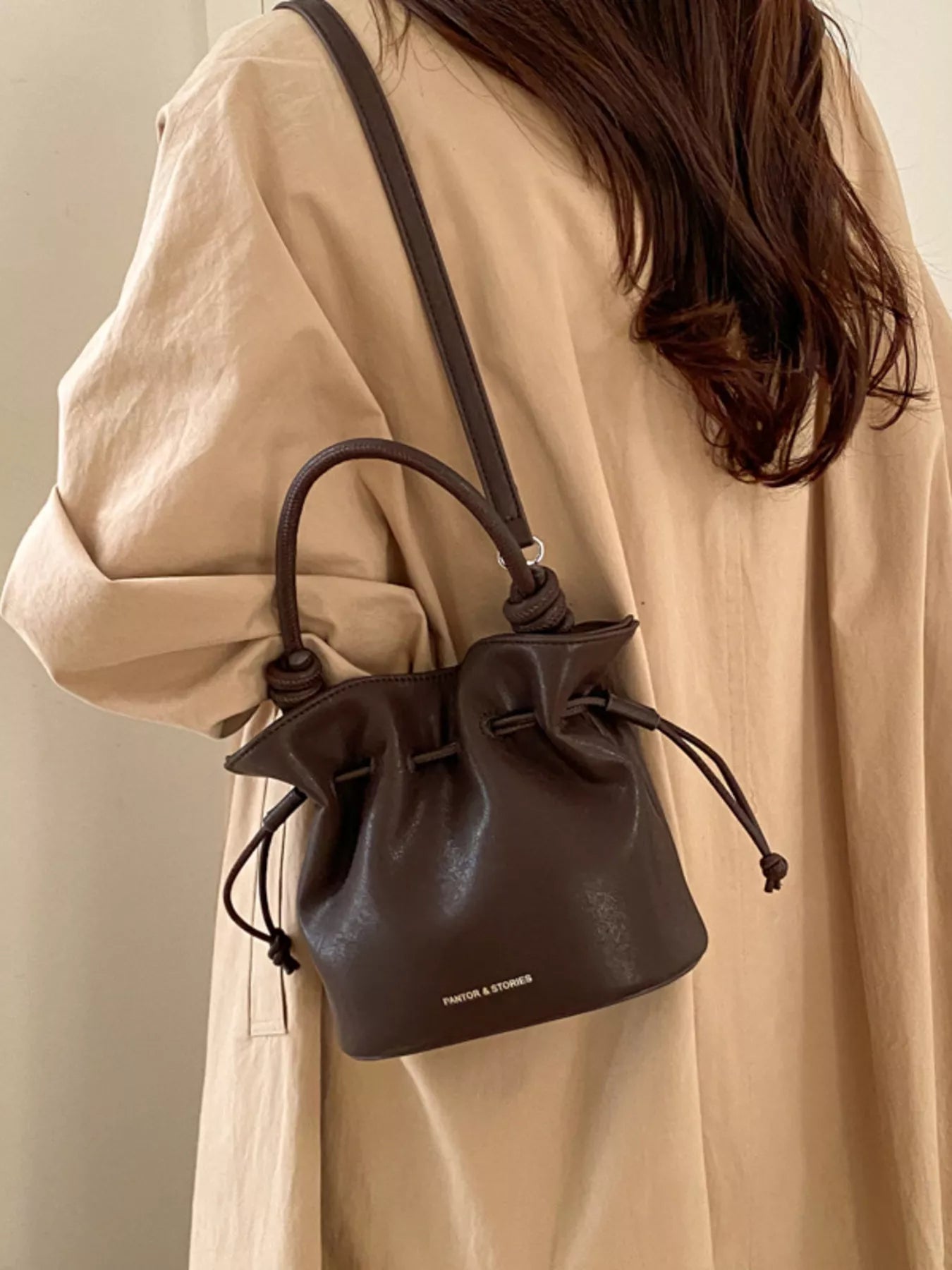 Person wearing a beige coat with a black leather bucket bag.