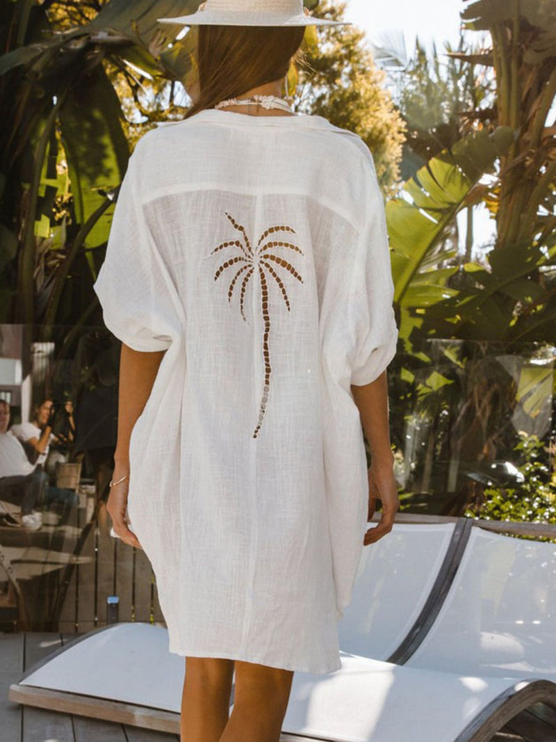 Person wearing a white cover-up with a palm tree design in a tropical setting