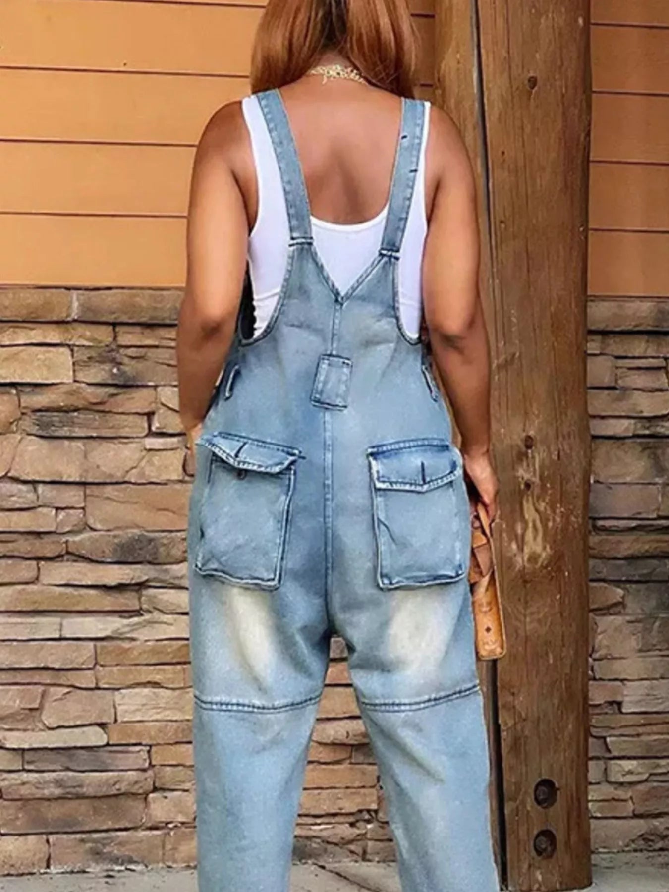 Person wearing light blue distressed overalls against a stone wall background