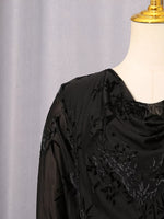 A close-up of a black sheer embroidered blouse displayed on a cream dress form mannequin against a light gray curtain background.