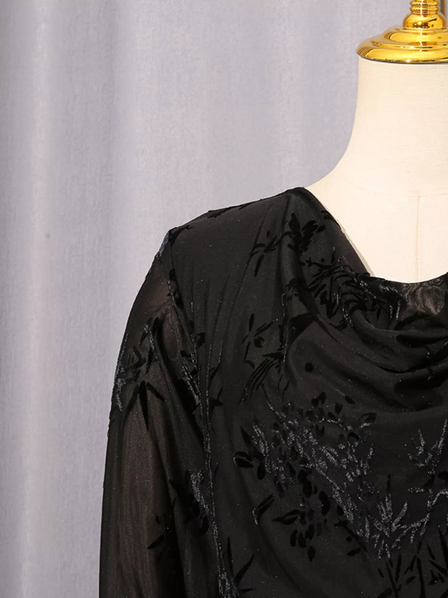 A close-up of a black sheer embroidered blouse displayed on a cream dress form mannequin against a light gray curtain background.