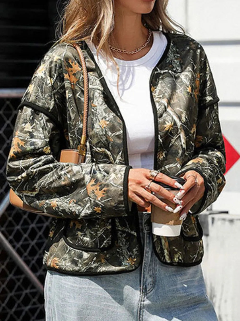 Person wearing a camouflage jacket holding a coffee cup outdoors.
