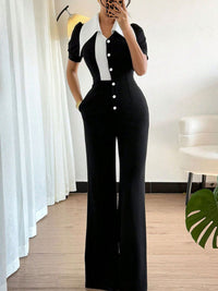 Person wearing a black and white jumpsuit in a room with white curtains and a chair.