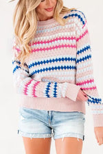 A woman wearing a pink knit sweater with horizontal blue and pink striped patterns, paired with light-wash denim shorts, against a plain white background.