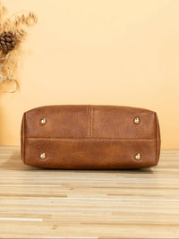Brown leather handbag with gold studs on a wooden surface and beige background