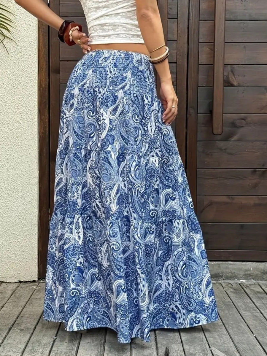 Person wearing a blue paisley patterned skirt with a white top against a wooden background.