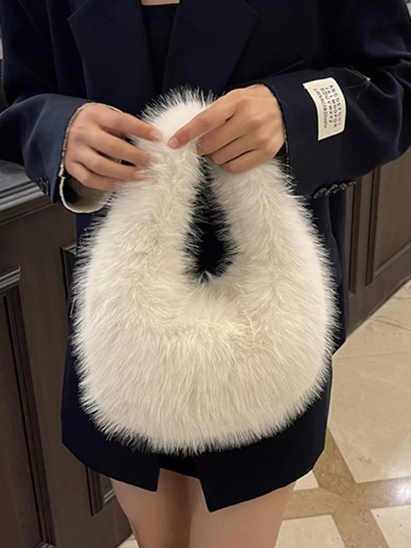 Person holding a fluffy white handbag with a dark coat.