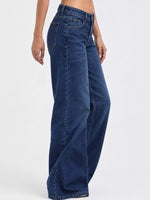 A person wearing dark blue wide-leg denim jeans, shown from the waist down against a plain light gray studio background.
