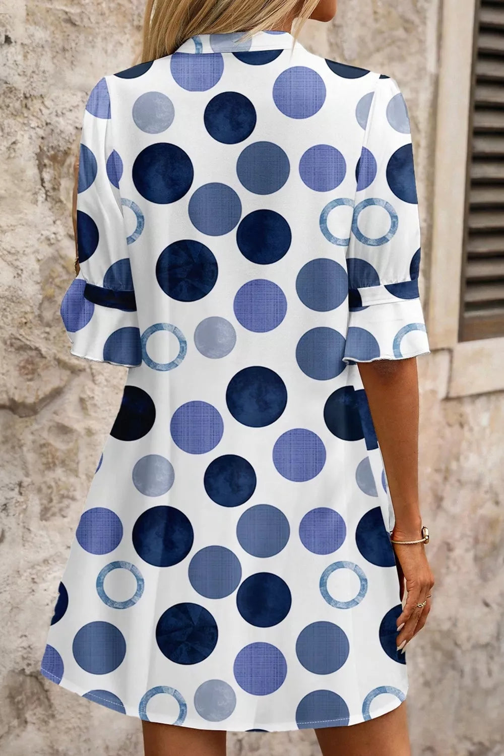 Woman wearing a polka dot dress with blue and white pattern against a stone wall.