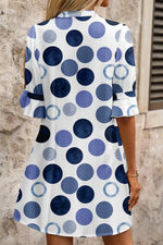 Woman wearing a polka dot dress with blue and white pattern against a stone wall.