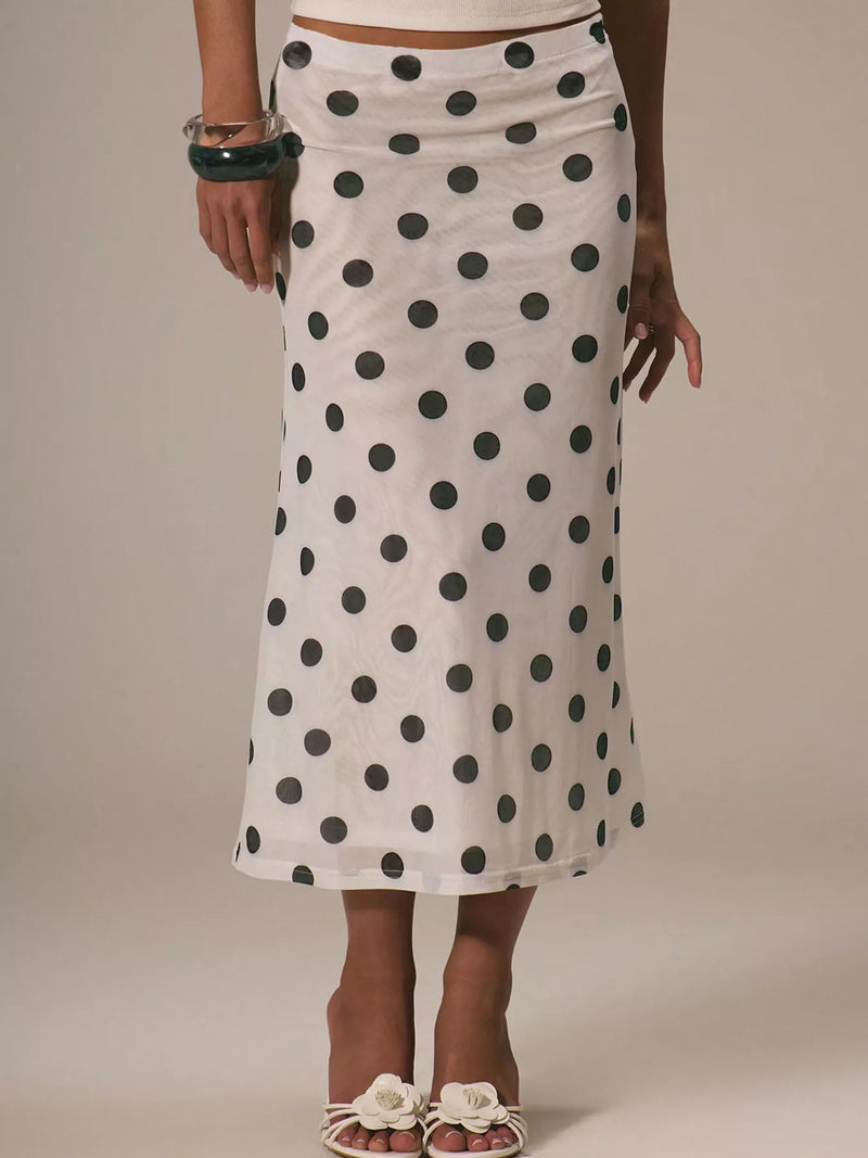 Person wearing a white skirt with black polka dots on a plain background