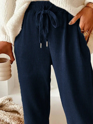 Navy ribbed pants worn with a white sweater, held by a person.