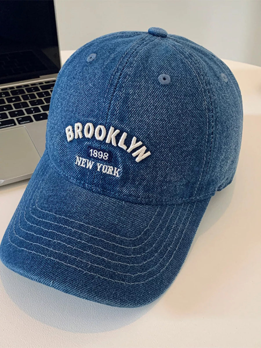 Blue cap with 'Brooklyn 1898 New York' text on a light surface.