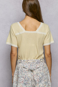 Woman wearing a light-colored top with lace trim and floral pants against a gray background