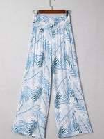 Tropical leaf patterned pants on a hanger against a gray background