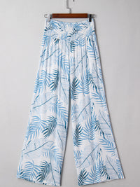 Tropical leaf patterned pants on a hanger against a gray background