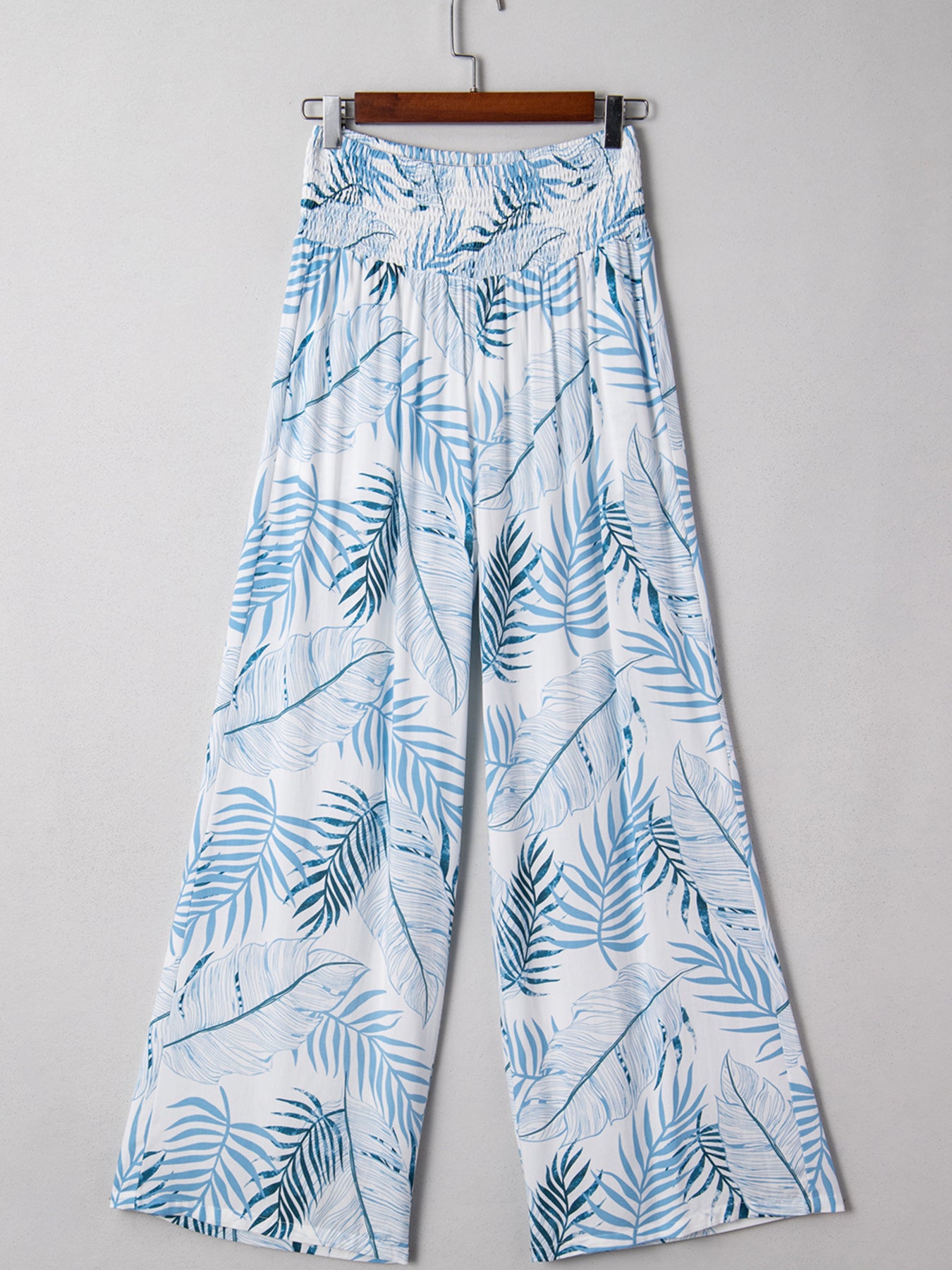 Tropical leaf patterned pants on a hanger against a gray background
