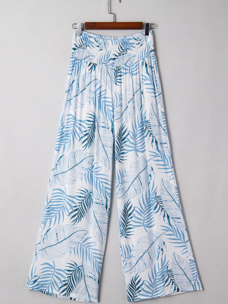 Tropical leaf patterned pants on a hanger against a gray background