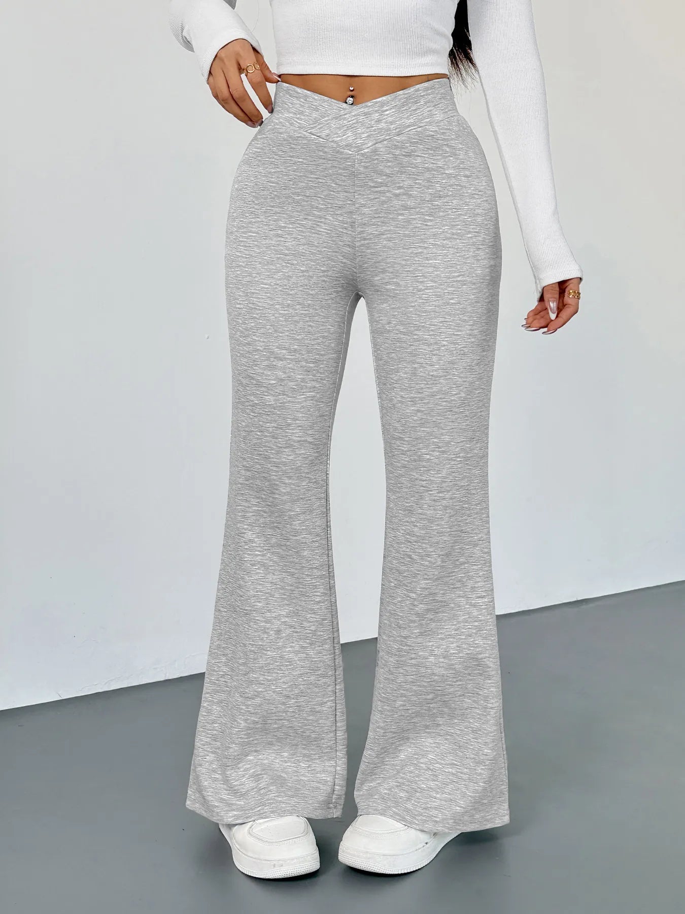 Person wearing gray flared pants and a white long-sleeve top on a plain background