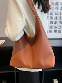 Brown leather handbag held by a person in an indoor setting