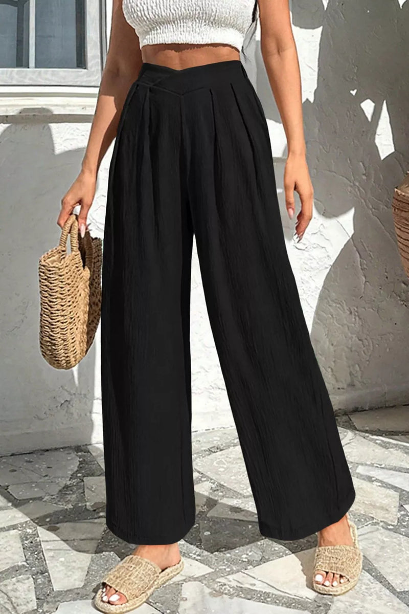 Person wearing black wide-leg pants and a white top, standing on a stone pavement.