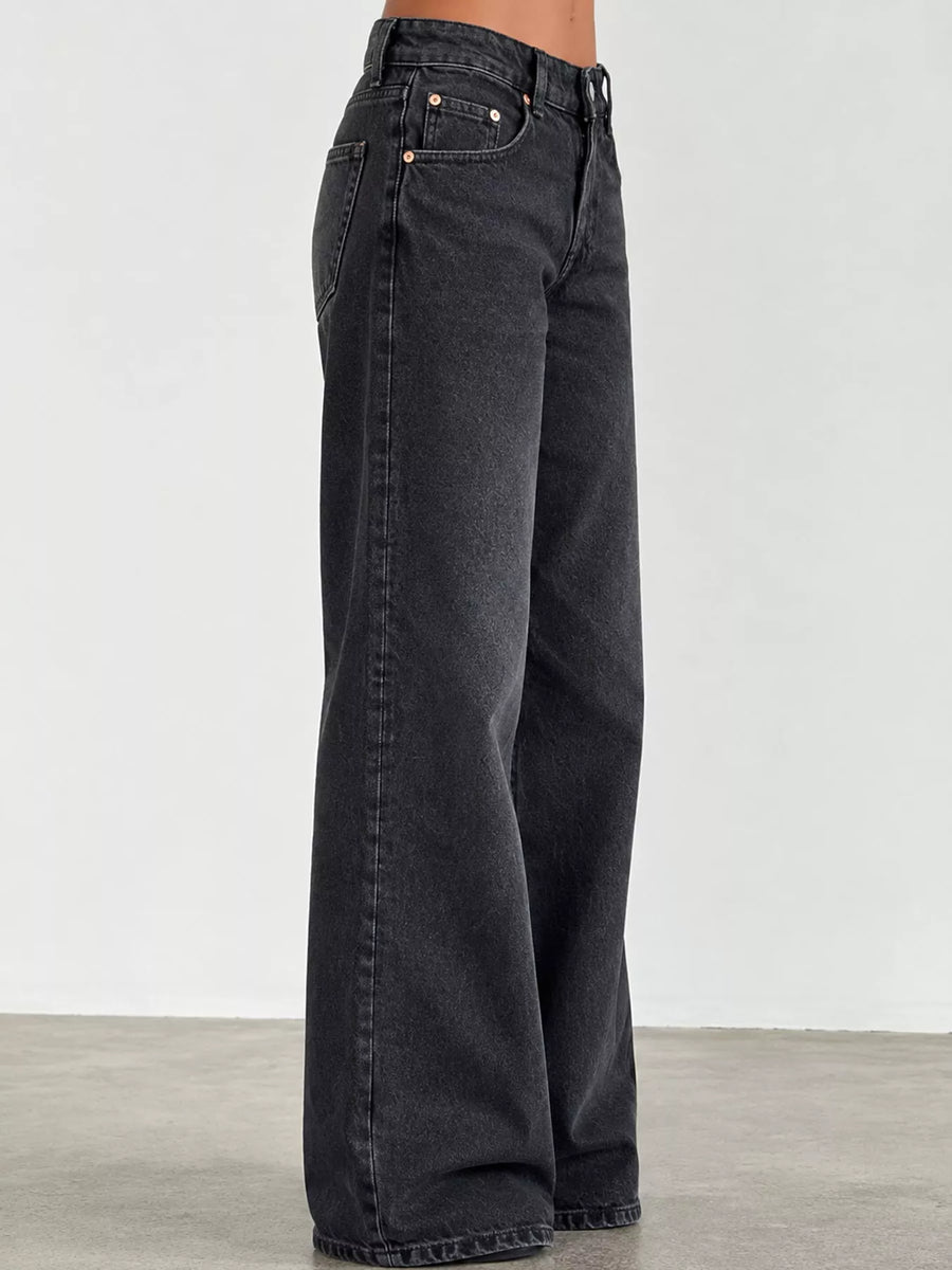 A person wearing dark charcoal gray wide-leg denim jeans, shown from the waist down against a plain light gray studio background.