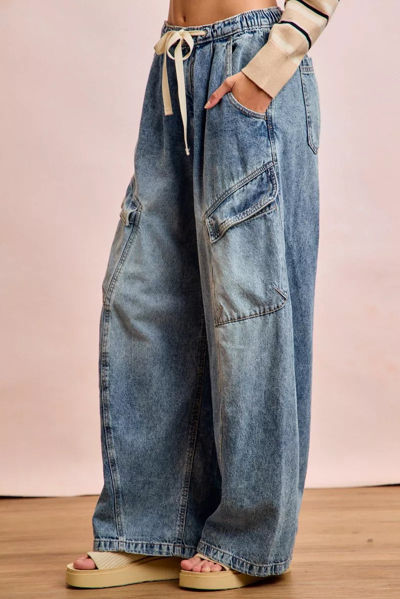 Wide-leg jeans worn by a person on a wooden floor with a pink background