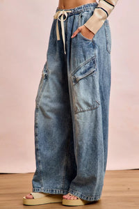 Wide-leg jeans worn by a person on a wooden floor with a pink background