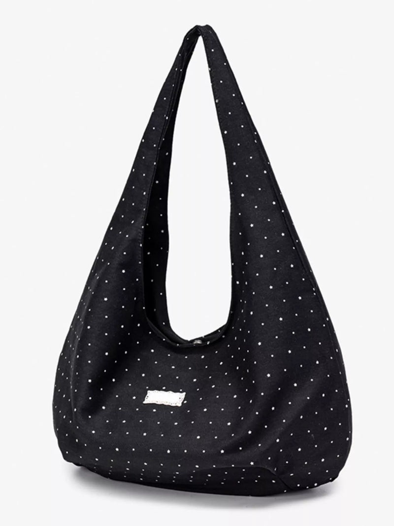 Black shoulder bag with white polka dots on a light gray background
