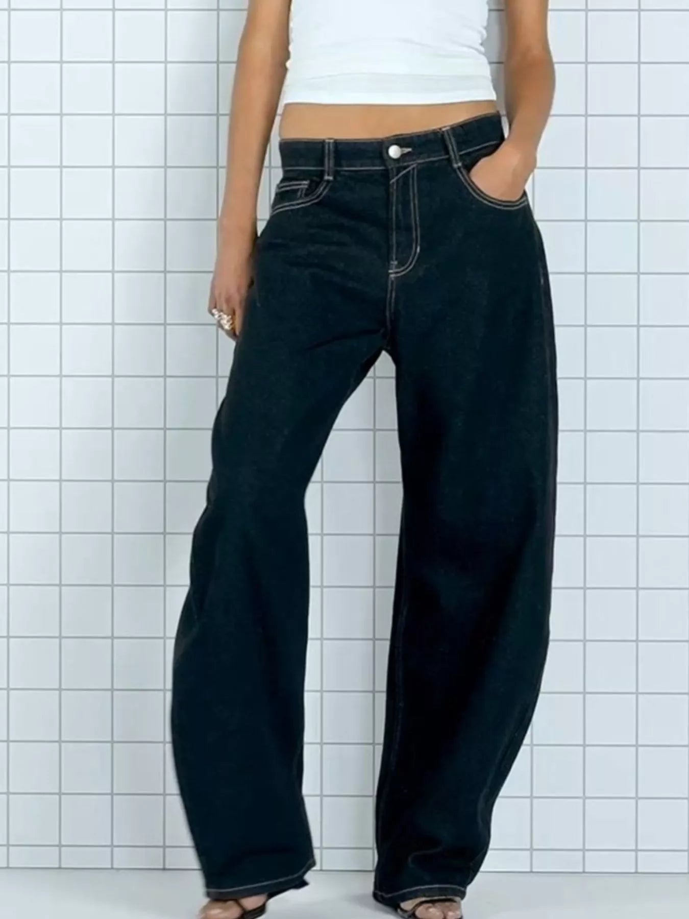 Person wearing black wide-leg jeans against a white tiled wall.