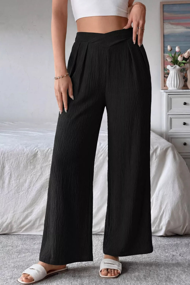 Person wearing black wide-leg pants and a white top in a bedroom setting.