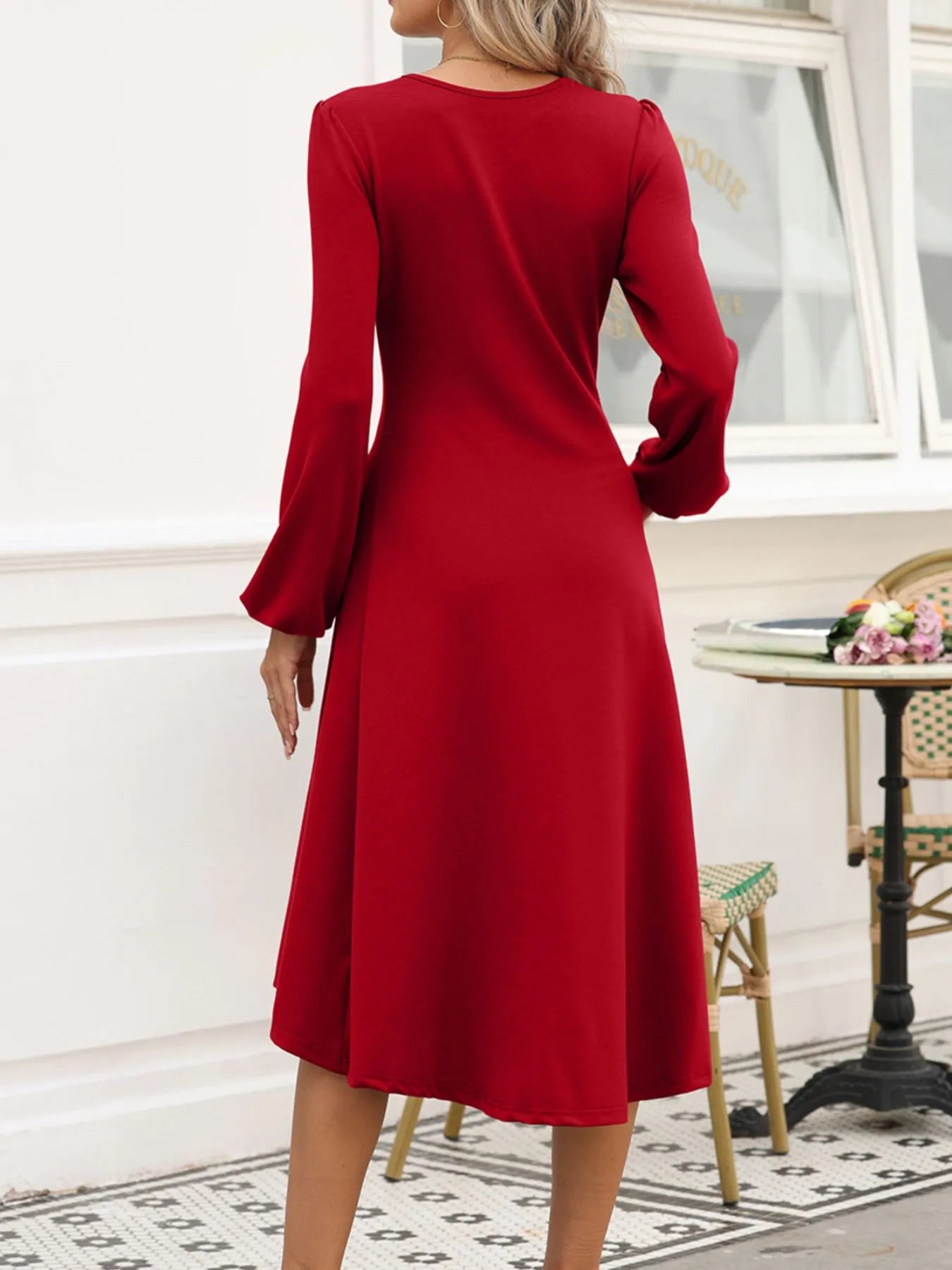 Red dress with long sleeves worn by a person, standing in a room with a table and chair.