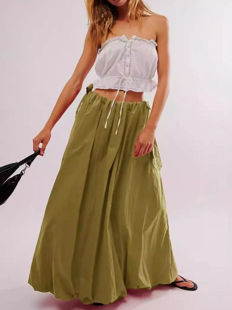 Woman wearing a white strapless top and green skirt against a plain background