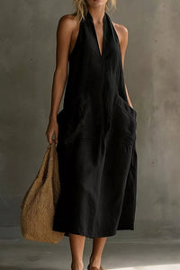 Woman wearing a black halter neck dress holding a brown bag against a gray background