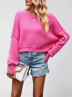 Person wearing a bright pink sweater and denim shorts holding a white handbag.
