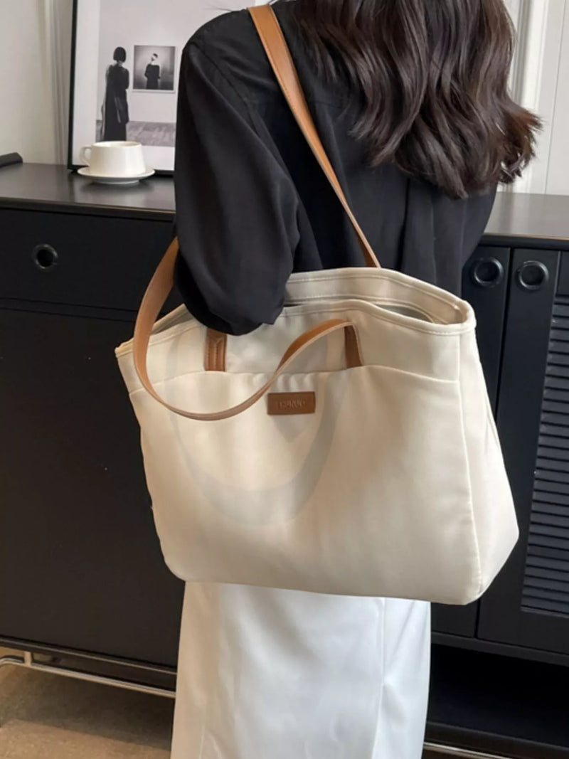 Person holding a beige tote bag with brown handles in an indoor setting.