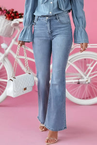 Person wearing blue jeans and a denim shirt with a white handbag, standing in front of a pink background with a bicycle.