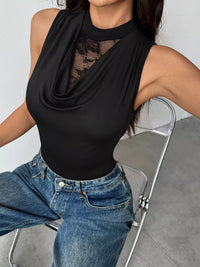 Person wearing a black sleeveless top with lace detail and blue jeans sitting on a chair.