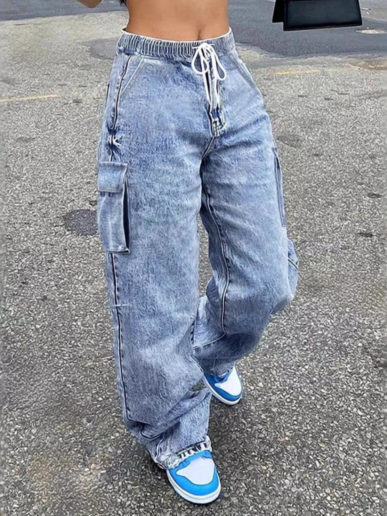 Person wearing acid-wash jeans and blue sneakers on a street.