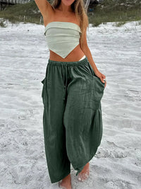 Person wearing a white top and green wide-leg pants on a sandy beach.