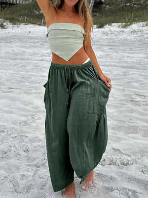 Person wearing a white top and green wide-leg pants on a sandy beach.
