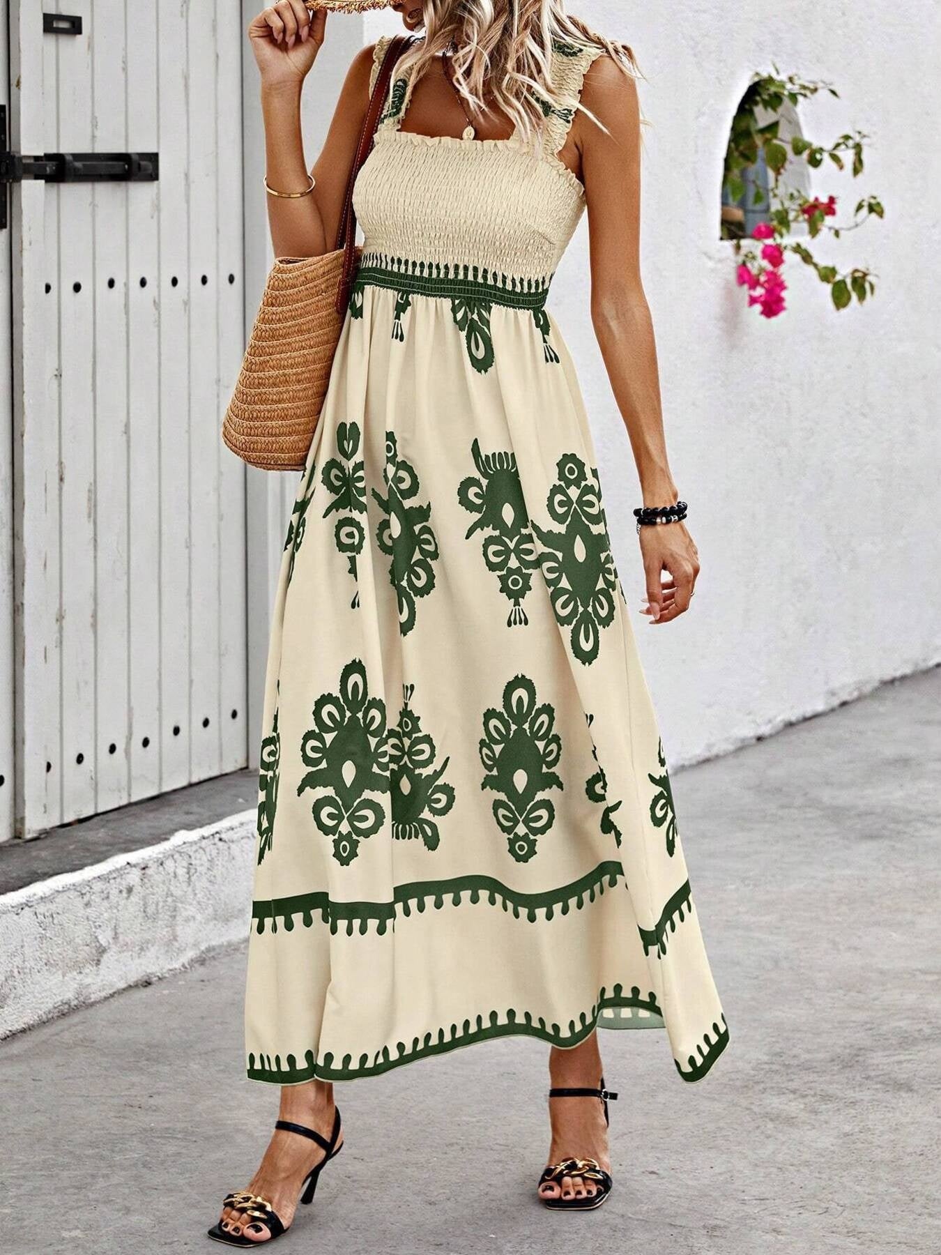 Woman wearing a beige dress with green patterns, standing against a white wall.