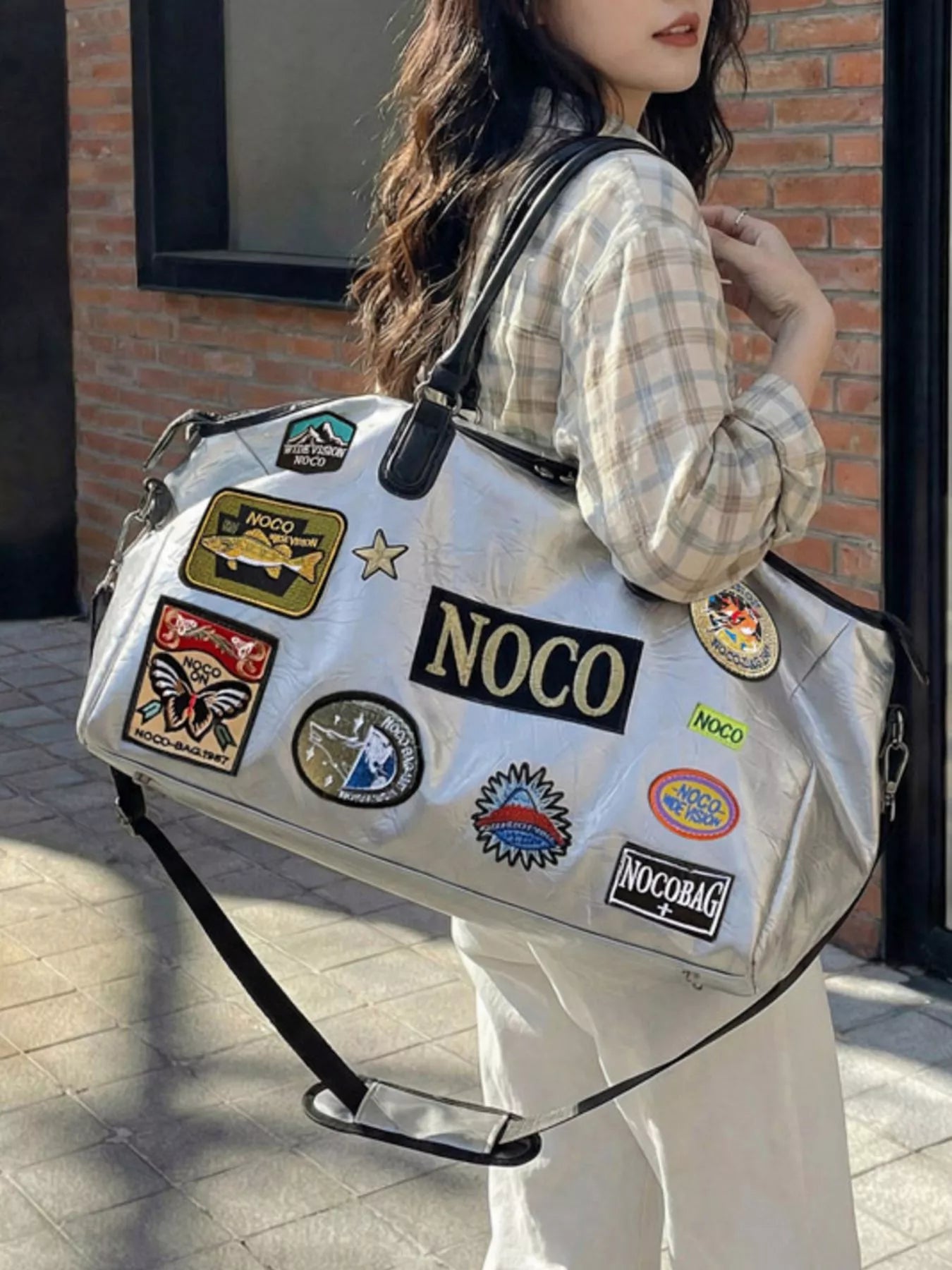 Person holding a white duffel bag with various patches, including 'NOCO'.