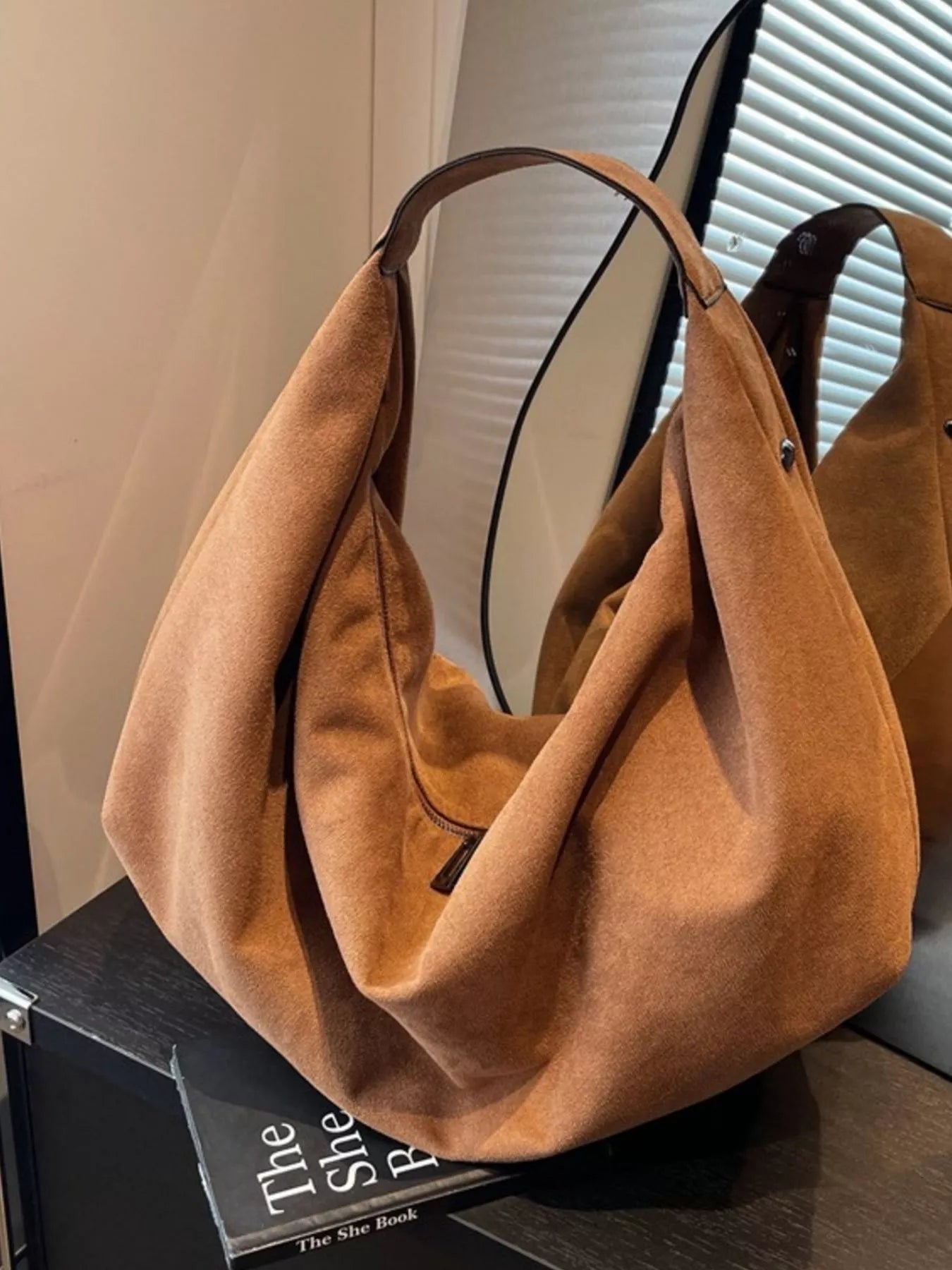 Brown suede handbag on a surface with a blurred background