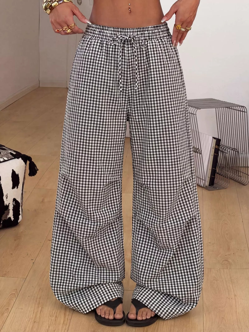 A person wearing loose, wide-leg checkered pants with a black and white gingham pattern, standing on a light wood floor in an indoor room.
