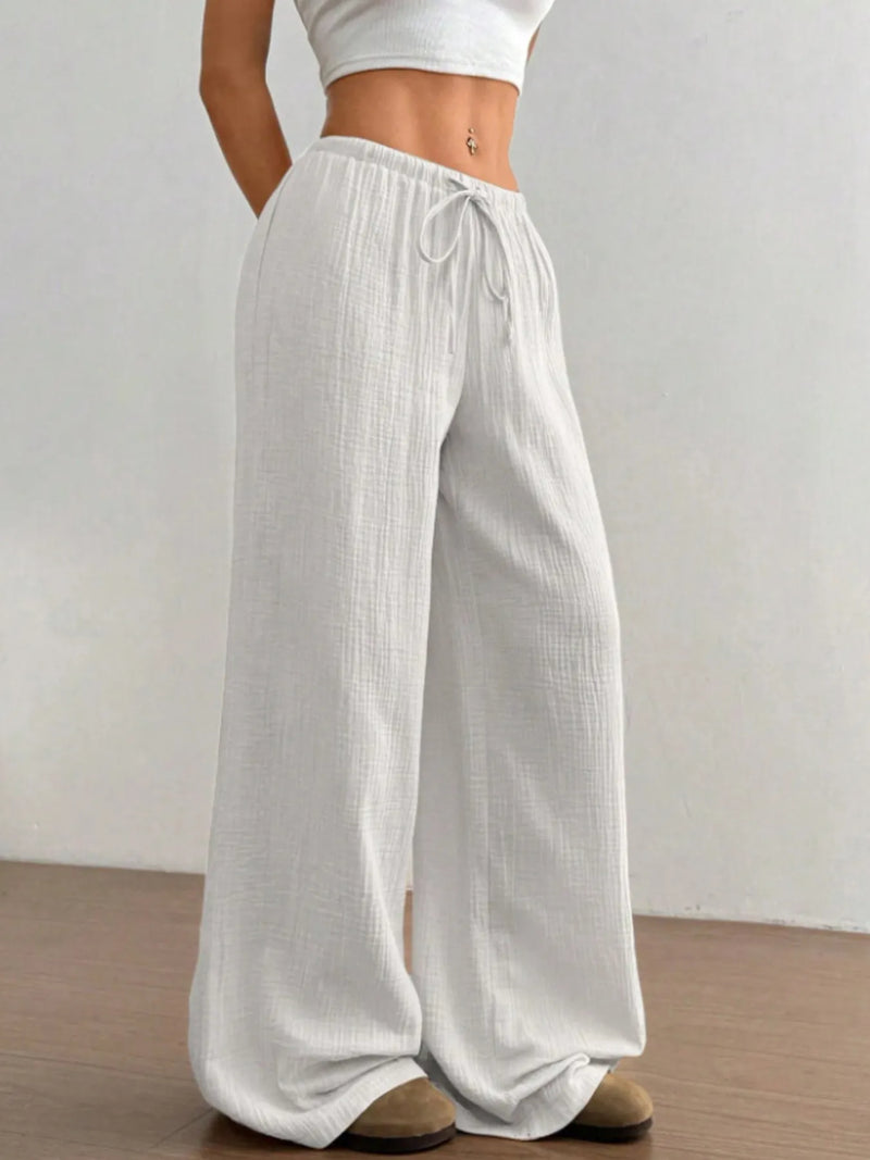 Person wearing light gray wide-leg pants with a white top on a plain background