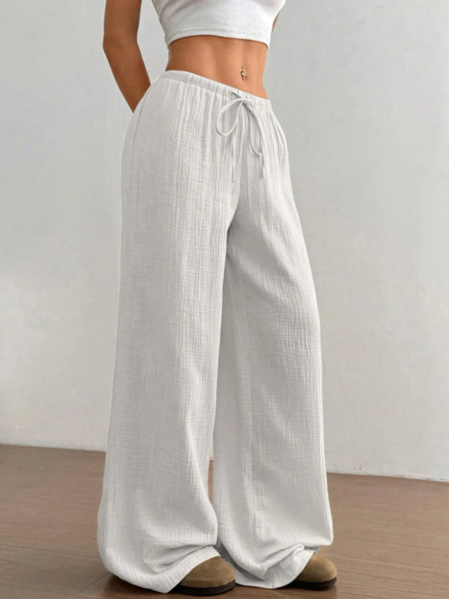 Person wearing light gray wide-leg pants with a white top on a plain background