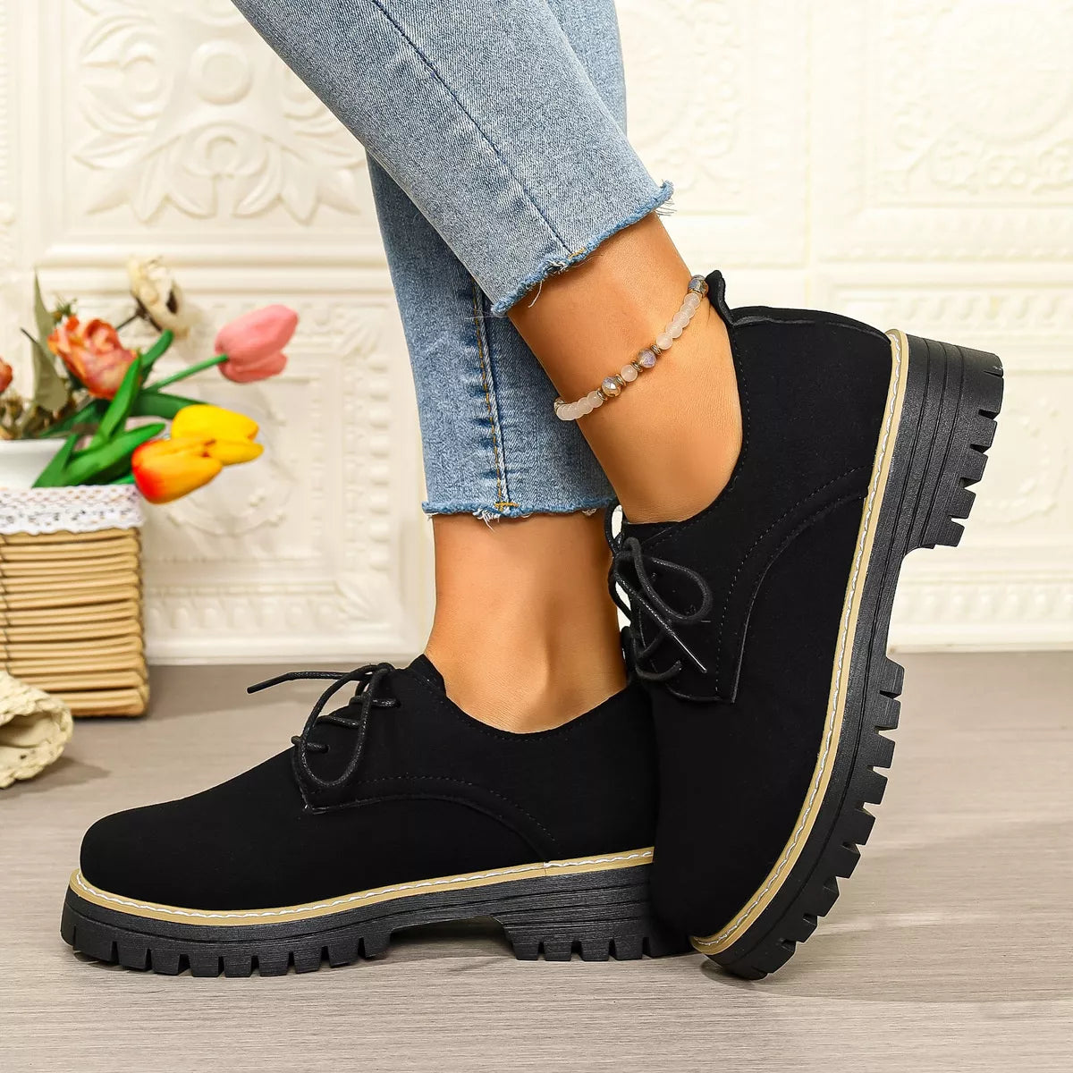 Black lace-up shoes worn with light blue jeans on a neutral background